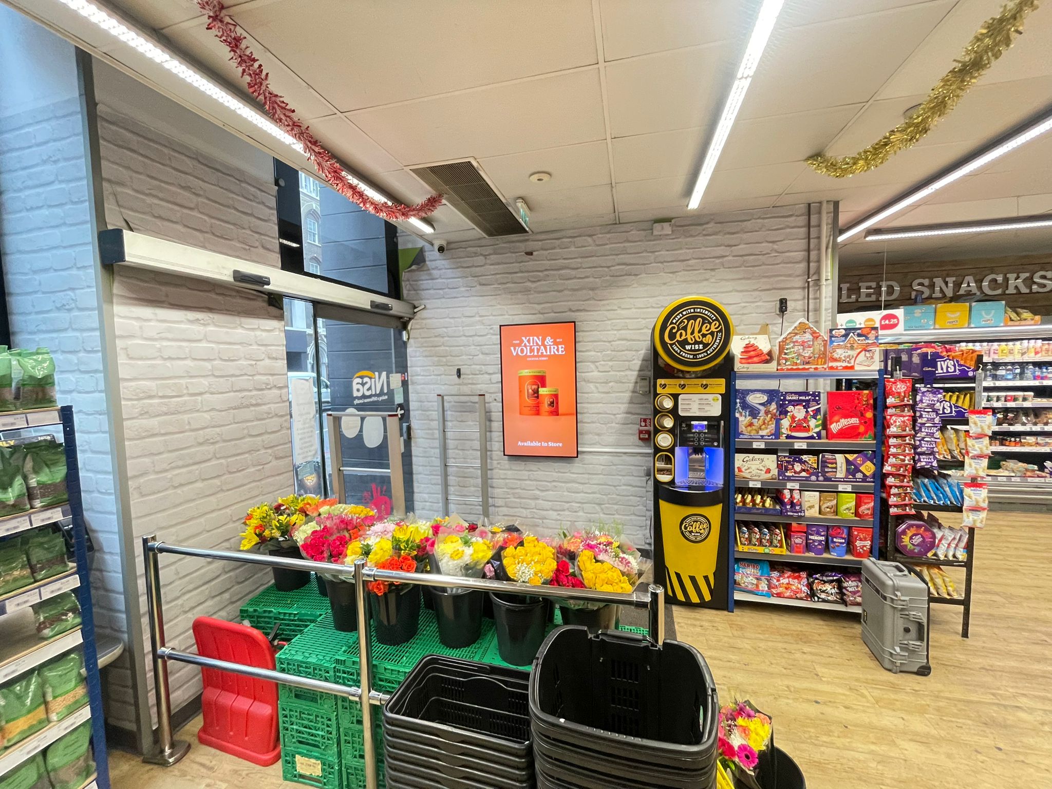Hanei wall-mounted screen running a Xin & Voltaire campaign in a Nisa convenience store