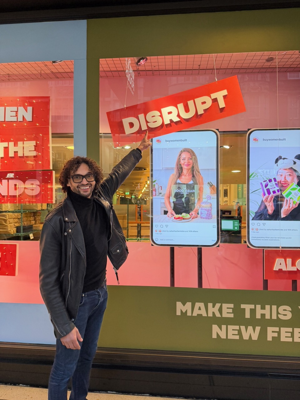 Hanei founder pointing at twin digital screens running a Buy Women Built campaign in the Whole Foods Kensington High Street window